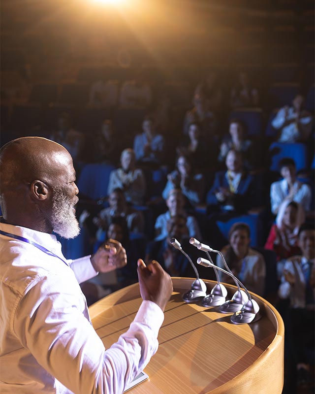 Sucessful man standing at podium speaking to large crowd in an auditorium