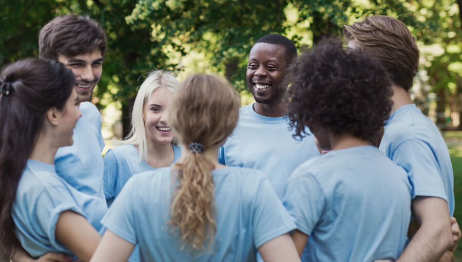 Group of oung adults in volunteer shirts stand arm-in-arm in a circle